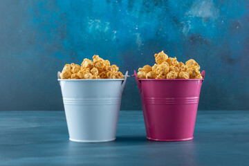 Two buckets filled with caramel coated popcorn on blue background