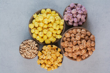 Various sized bowls with servings of colorful popcorn candy on marble background