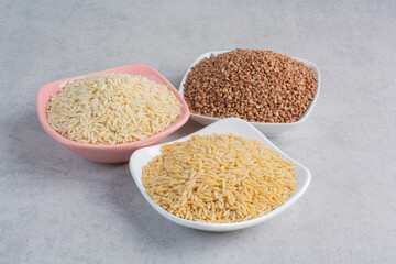Short grain and long grain rice piled on platters next to a platter of buchwheat on marble background