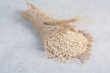 Heap of wheat grain wrapped in a piece of cloth on marble background - obrazy, fototapety, plakaty
