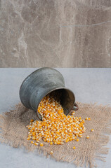 Corn spliing out of a small metal jug fallen over on a piece of cloth on marble background