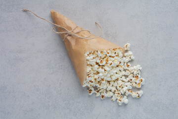 Popcorn spilling out of tied paper wrapping on marble background