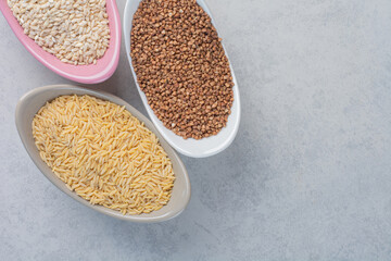 Three bowls with rice, wheat and buckwheat on marble background