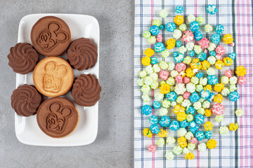 Pile of popcorn candy on a towel next to a platter of cookies on marble background