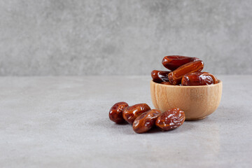A small bowl of dates next to a handful on marble background