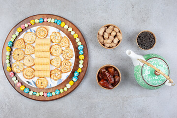 Teapot, small bowl of tea leaves and dates and a tray of cookie chips and popcorn candy on marble background