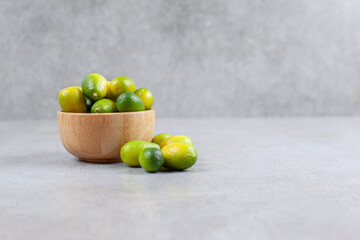Kumquats inside and next to a wooden bowl on marble background
