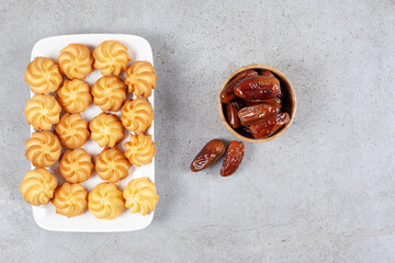 A small serving of dates with a full plate of cookies on marble background