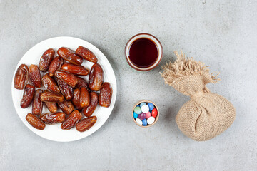 A platter of dates, a cup of tea, a sack and a small bowl of candies on marble background