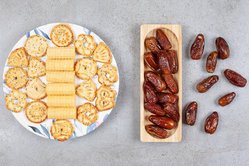 A serving of biscuits on a painted platter with a pile of dates on and next to a wooden tray on marble background