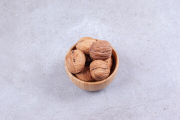 A handful of walnuts piled in a wooden bowl on marble background