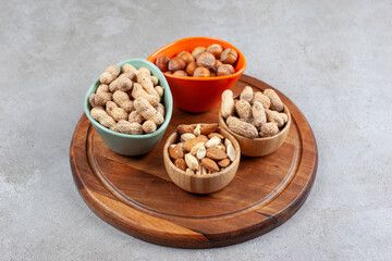 Assorted nuts neatly piled into four bowls on a wooden tray on marble background