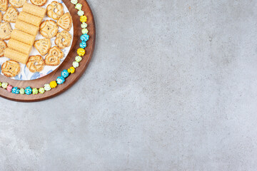 Plate of various cookies encircled by popcorn candy on wooden board on marble background