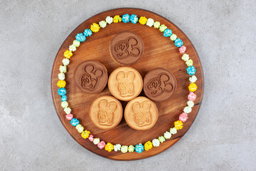 Cookies encircled with candies on wooden board on marble background