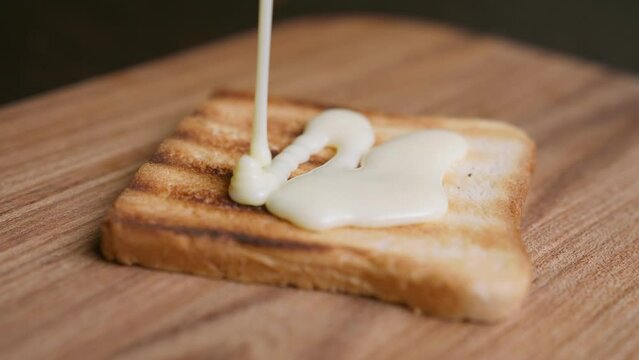 Pouring condensed milk cream over toasted white wholegrain bread. Macro shot