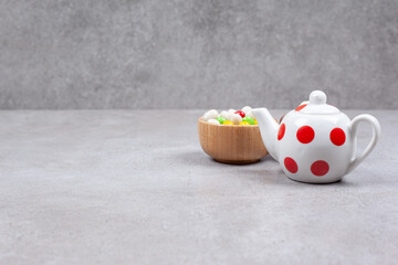 A small teapot with a bowl of candy on marble background