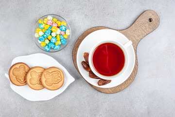 Cup of tea with dates on wooden board by a bowl of popcorn candy and a plate of cookies on marble background