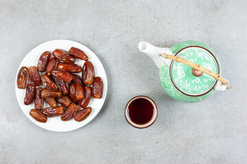  A cup of tea and an ornate teapot next to a plate of fresh dates on marble background