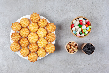 Bowls of mullberries, candies and peanuts homemade cookies on a plate on marble background