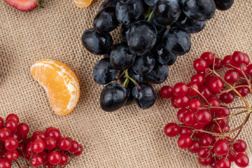 Composition of grapes, strawberry slice, redcurrant and tangerine slices on textile background