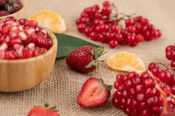 Bowls of pomegranate and raspberry with an assortment of fruits scattered on textile background
