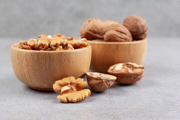 Two bowls of whole and cracked walnuts on marble background