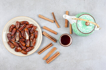  A cup of tea, scattered cinnamon cuts and an ornate teapot next to a plate of fresh dates on marble background