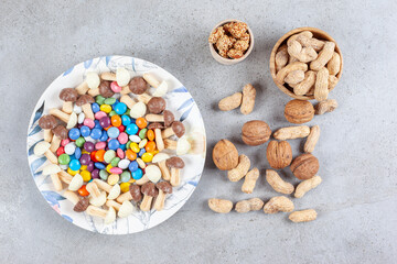 Plate of candies and chocolate mushrooms with scattered bowl of nuts on marble background