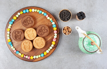 Cookies and a circle of candies on a wooden board next to bowls of peanuts, tea and mullberries and a teapot on marble background