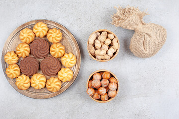 A wooden tray of cookies next to bowls of hazelnut and chocolate mushrooms and a sack on marble background