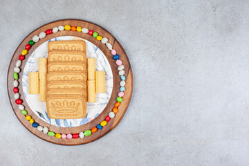 Biscuits lined up on a plate and surrounded by candies on wooden board on marble background