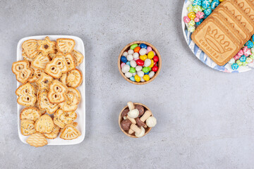 Two plates of biscuits with bowls of candy and chocolate mushroom in the middle on marble background