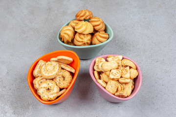 Various biscuits and cookies in colorful bowls on marble background