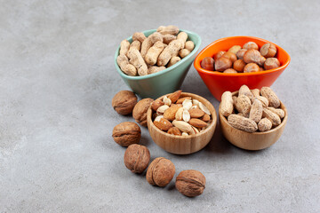 An assortment of various nut types in wooden bowls on marble background