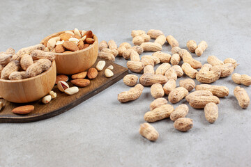 Assortment of nuts in bowls on wooden board and scattered on marble background