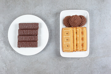 Plate of chocolate waffles next to plate of biscuits on marble background