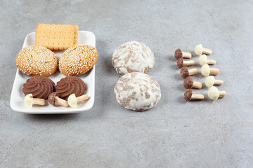 Plate of assorted cookies next to russian gingerbread and mushroom chocolates on marble background