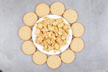 Plate full of cookie chips surrounded by biscuits on marble background