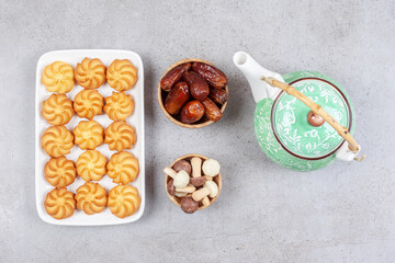 Plate of biscuits next to ornate teapot and bowls of dates and mushroom chocolates on marble background