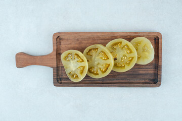 Pickled green tomato slices on wooden board