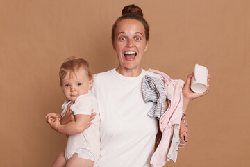 Extremely happy young mother with bun hairstyle holding her toddler daughter and screaming happily,...