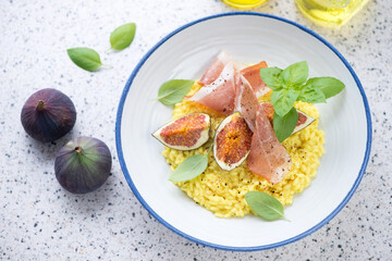 Plate of risotto with figs, prosciutto and basil on a light-grey granite background, elevated view, horizontal shot