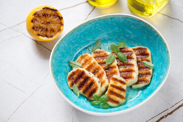 Turquoise bowl with slices of grilled halloumi cheese, studio shot on a light-beige stone background