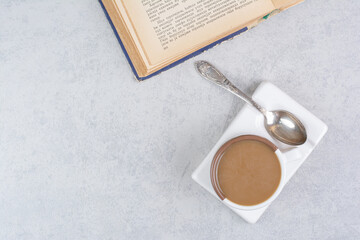 Cup of milk coffee, spoon and book on stone surface