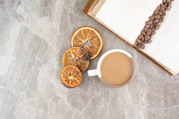 Coffee beans on book with cup of coffee and orange slices