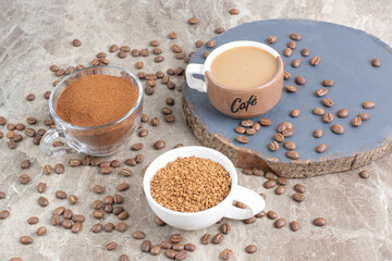 Cup of coffee, coffee beans and ground coffee on marble surface