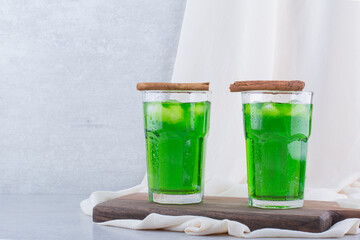 Two glasses of tarragon juice with ice on wooden board