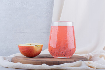 A glass of juice with seeds and apple slice on wooden board