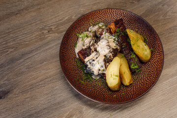 Roast meat cutlet beef with potato, pepper in white sour sauce with greenery on plate on cafe or restaurant table. Top