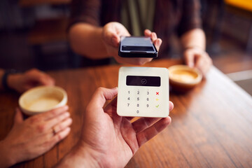 Close Up Of Customer Making Contactless Payment In Coffee Shop Using Mobile Phone